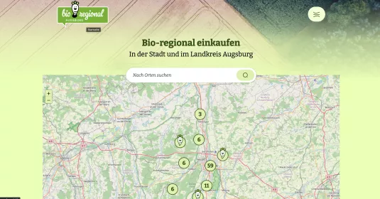 Die Homepage der Seite von bio regional augsburg. Darauf zu sehen ein grüner Hintergrund, bei dem etwas ausgeblasst ein Feld aus der Vogelperspektive zu sehen ist. Darunter folgt die Überschrift "Bio-regional einkaufen in der Stadt und im Landkreis Augsburg". Darunter wird den Nutzer*innen eine Karte angezeigt mit einer Suchfunktion. 