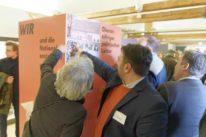 Interessierte Menschen deuten auf ein Foto auf einer Ausstellungssäule im Museum von Egling - Ein Ausstellungsdesign von elfgenpick Werbeagentur in Augsburg